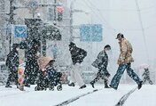 降りしきる雪の中、足早に横断歩道を渡る人たち＝１８日午後０時２０分ごろ、富山市中央通り