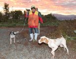 朝焼けに染まる空の下、猟犬を伴って河川敷を歩くハンター＝１５日午前６時半ごろ、富山市町袋の常願寺川左岸