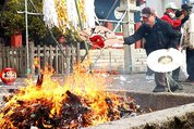 天狗の面をあしらった飾りを火の中に投げ入れる住民