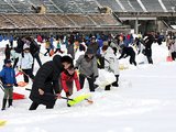 膝ほどの高さまで雪が積もったピッチを除雪する大勢の人