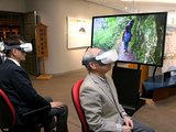 ゴーグルを着けて下ノ廊下のＶＲ映像を体験する運営委員。モニターでも下ノ廊下を紹介している＝黒部市歴史民俗資料館