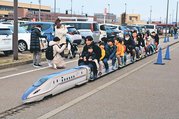 ミニ新幹線の乗車を楽しむ子どもら。左奥は北陸新幹線新高岡駅